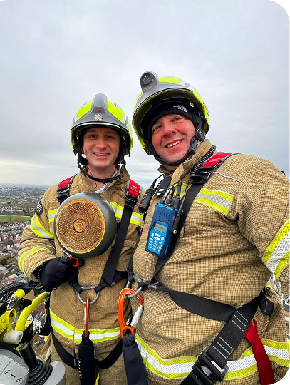 Two firefighters in safety gear posing at height.